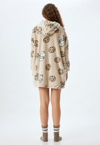Manta con capucha de felpa beige con motivos de galletas y leche. Presenta una capucha, mangas largas y un diseño hasta las rodillas. Textura suave.