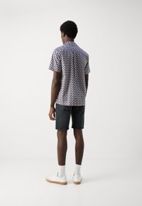 Camisa de manga corta con un patrón de lunares azul marino sobre un fondo crema, combinada con pantalones cortos oscuros y zapatillas blancas. Textura de tela suave.