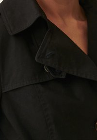 Czarny płaszcz trench z dużym kołnierzem, podwójnym zapięciem na guziki i gładką teksturą, ukazujący klasyczny element designu.