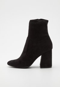 Černé semišové kotníkové boty s špičatou špičkou, vysokým blokovým podpatkem a prošívanými detaily. Boční zip pro snadné obouvání.
