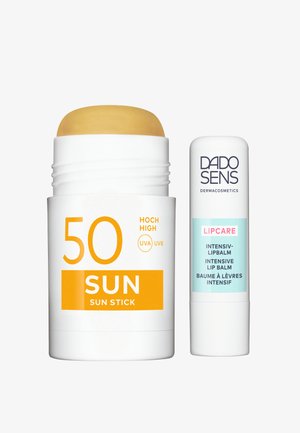 Sonnenschutzstick mit gelbem Deckel und weißem Tube, beschriftet mit "50 SUN", neben einem weißen Lippenbalsamstick mit blauen und schwarzen Akzenten, beschriftet mit "DADO SENS."