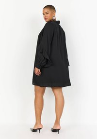 Rochie neagră, cu mâneci lungi și voluminoase și guler; confecționată dintr-un material ușor, prezintă o croială lejeră. Tocuri cu accente decorative.