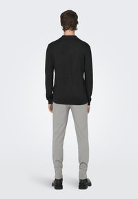 Schwarzer Pullover mit langen Ärmeln und gerippten Bündchen, kombiniert mit hellgrauen Hosen. Rückansicht eines Mannes, der schwarze Schuhe trägt, vor einem einfarbigen Hintergrund.