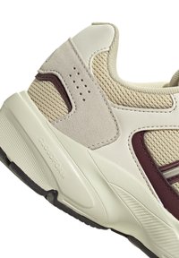 Sneaker mit einem beigen Textilobermaterial, Wildlederelementen, bordeauxroten Details und einer strukturierten Gummisohle. Verfügt über Perforationen für bessere Atmungsaktivität.