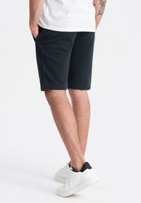 Shorts bleu marine foncé en tissu doux, dotés de poches latérales et d'une taille élastique, associés à des baskets blanches avec des accents noirs.