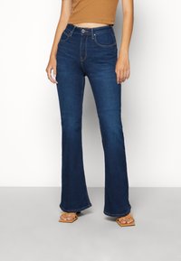 Uppskurna mörkblå denimjeans med framfickor, fem bältesöglor och kontrasterande sömmar, kombinerade med bruna skor.