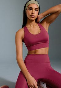 Top sportivo corto color borgogna e leggings a vita alta in tessuto elastico e liscio. Un cerchietto verde chiaro completa l'outfit.