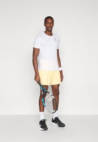 Λευκό κοντομάνικο αθλητικό μπλουζάκι, κίτρινες σορτς, μαύρα αθλητικά παπούτσια, κρατώντας ένα ρακέτα τένις. Απλός σχεδιασμός, ελαφρύ ύφασμα και αντίθετα χρώματα.