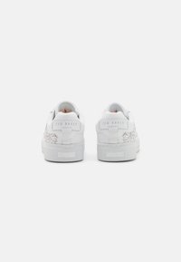 Zapatillas de cuero blanco con un diseño texturizado, sutiles acentos florales y marca en el talón. Suela de goma, estilo bajo.
