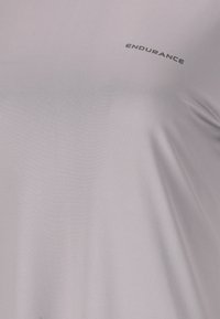 Ljust grå idrottströja med ordet "ENDURANCE" tryckt nära övre bröstet på en slät tyg.