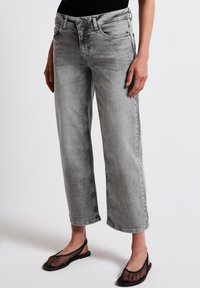 Jeans de mezclilla gris con un corte relajado, que presentan detalles metálicos y una cintura de altura media. Pernera recortada con un corte recto y un desgaste mínimo.