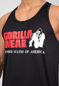 Juodas marškinėlis be rankovių, pagamintas iš lengvos medžiagos, su ryškiu raudonu ir baltu užrašu „GORILLA WEAR“ ir „JAV“, su gorilos grafika.