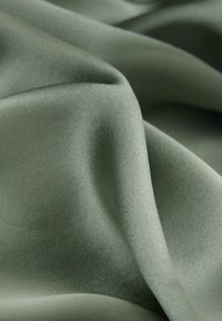 Zachte, gladde stof in een gedempte groene tint, met zachte plooien en een zijdezachte textuur, ideaal voor verschillende textieltoepassingen.