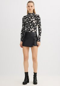 Top negro de manga larga con estampado floral y cuello alto, combinado con una minifalda negra de cuero con detalle de solapa frontal. Botines negros hasta el tobillo.