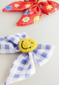 Håraccessoarer: en röd tygrosett med färgglada mönster, och en blå och vit rutig rosett med ett lurvigt gult smiley-ansikte.