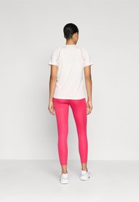 Witte sport T-shirt met roze accenten, gecombineerd met strakke roze leggings met een subtiele textuur. Model draagt witte sportschoenen.