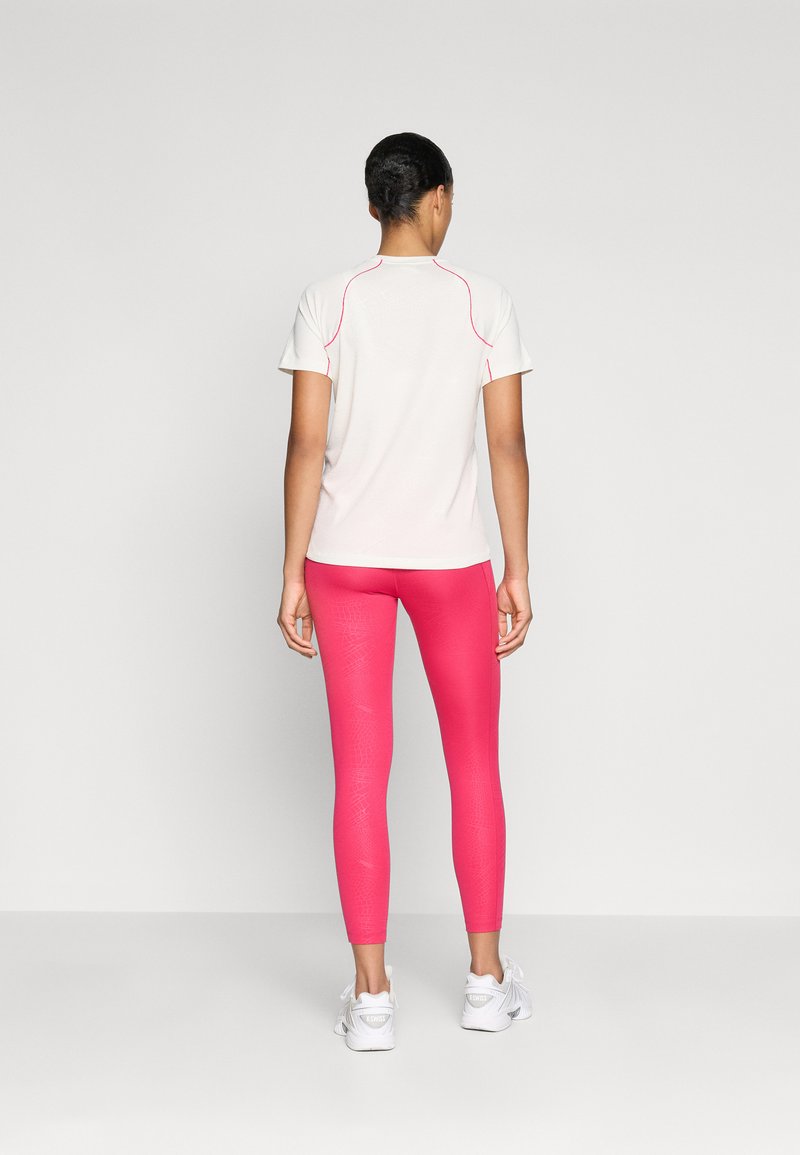 White athletic t-shirt with pink accents, paired with fitted pink leggings featuring a subtle texture. Model wears white athletic shoes.