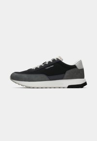 Low-profile Calvin Klein sneaker in black, dark gray, and white suede and mesh with white sole and gray laces, side view on white background.