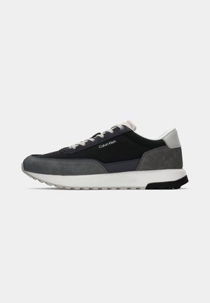 Laagprofiel Calvin Klein sneaker in zwart, donkergrijs en witte suede en mesh met witte zool en grijze veters, zijaanzicht op witte achtergrond.