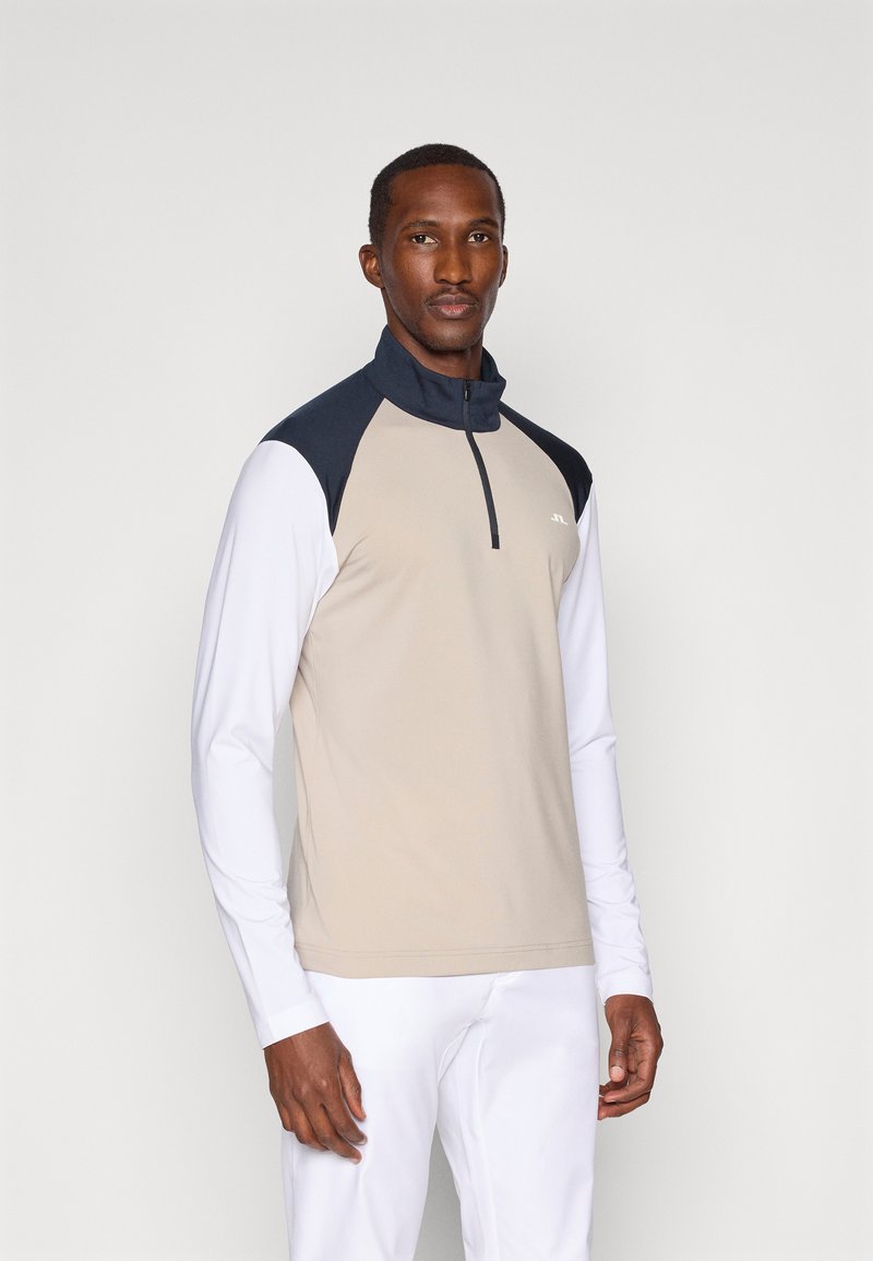 Μπεζ μισό φερμουάρ μπλούζα μακρύ μανίκι με σκούρες μπλε λεπτομέρειες στους ώμους, φτιαγμένη από απαλό ύφασμα. Διαθέτει φερμουάρ στον λαιμό και λευκά μέρη στα μανίκια.