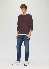 Fioletowy sweter o teksturowanym splocie, biała koszulka pod nim, niebieskie dżinsy i jasnoszare trampki z ciemnymi akcentami. Prosty, casualowy strój.