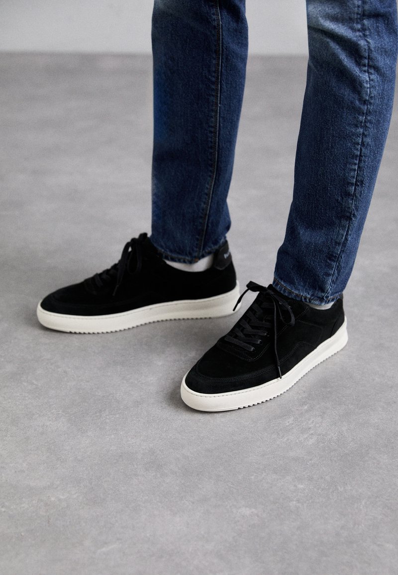 Black suede sneakers with a white rubber sole, featuring a classic low-top design, rounded toe, and flat black laces.