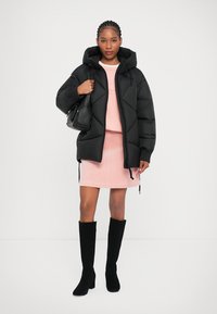 Čierna puffer bunda s prešívaným dizajnom, ružová šaty na sveter, čierne vysoké čižmy a malá čierna kabelka.