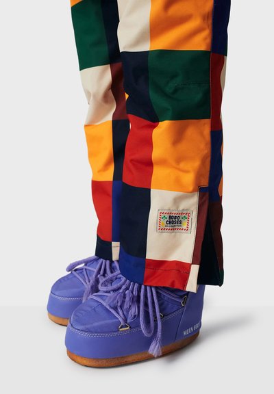 Farverige patchworkbukser i forskellige nuancer med et tag, parret med lavendel høje sneakers med en tekstureret sål og unikke snørebånd.