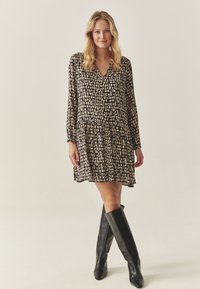 Juodos ilgos rankovės suknelė su daugiasluoksne sijonu, dekoruota kreminiu abstrakčiu raštu. Suderinta su kelių ilgio juodais odiniais batais.