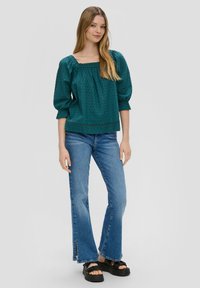 Türkise, strukturierte Bluse mit quadratischem Ausschnitt und Puff�ärmeln, kombiniert mit ausgestellten blauen Jeans und schwarzen Plateausandalen.