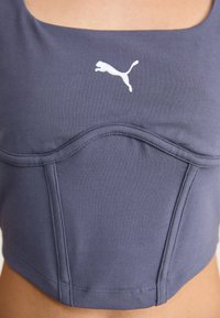 Marineblauwe cropped top van gladde stof. Kenmerkt zich door een vierkante halslijn, naden aan de voorkant en een witte Puma-logo gedrukt op de borst.