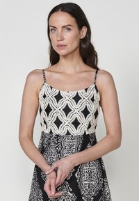 Robe noire et blanche avec un haut ajusté présentant un corsage texturé et à motifs, ainsi qu'une jupe fluide aux motifs complexes. Les bretelles spaghetti sont incluses.