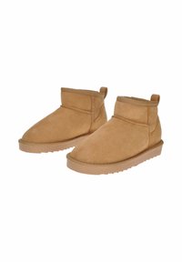 Stivaletti alla caviglia in suede marrone chiaro con punta arrotondata, cuciture minime e un gambale corto e flessibile. Presentano una suola in gomma testurizzata e un occhiello sul retro per facilitare l'indosso.