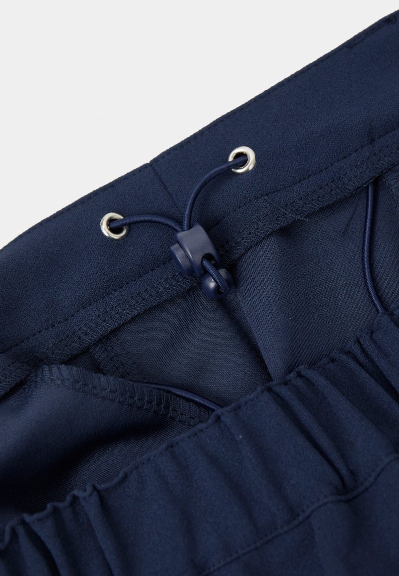 Marineblauwe elastische tailleband met verstelbare trekkoord en plastic toggle op een paar broeken of shorts.