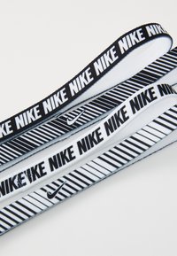 Trys Nike elastingos juostos juodos ir baltos spalvų. Viršutinė ir apatinė juostos turi pakartotinį tekstą; vidurinė turi dryžuotą raštą.
