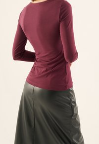 Vinröd långärmad topp med rund hals, kombinerad med en svart kjol i konstläder. Slät textur, figurnära silhuett och enkel design.