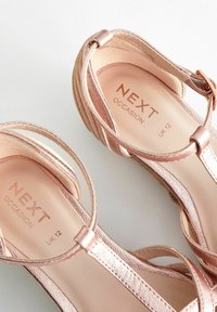 Sandales compensées métalliques couleur or rose avec brides, boucle à la cheville et semelle en liège, étiquetées Next Occasion, taille UK 12, sur fond blanc.
