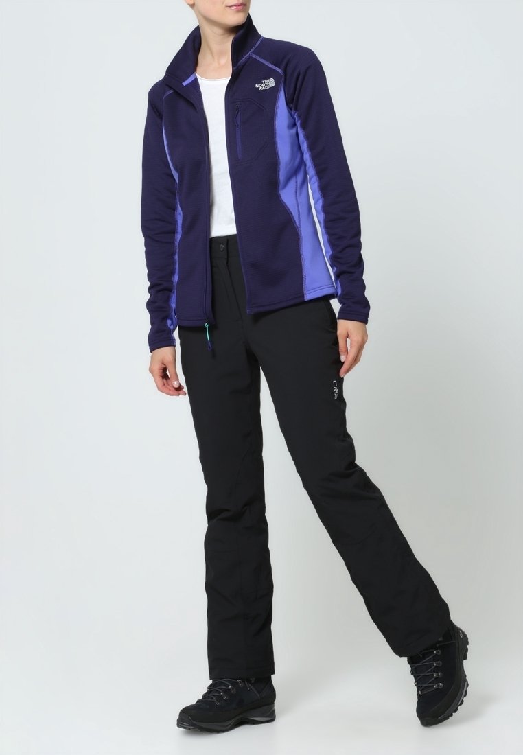 Polarowa kurtka w ciemnofioletowym kolorze z jasnofioletowymi akcentami, z kieszenią na zamek i wysokim kołnierzem; zestawiona z czarnymi spodniami i solidnymi butami.