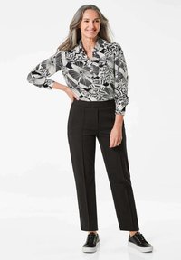 Zwart-witte bloempatron blouse met een kraag, gecombineerd met op maat gemaakte zwarte broek en zwarte sneakers met witte zolen.