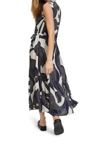 Femme marchant dans une robe sans manches, longue jusqu'aux chevilles, à imprimé floral abstrait noir et blanc, et portant des chaussures noires sans lacets.
