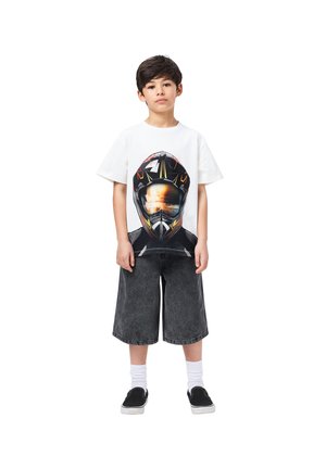 Λευκό T-shirt κοντό μανίκι με γραφικό σχέδιο ενός κράνους. Συνδυασμένο με σκούρες γκρι φαρδιές βερμούδες και μαύρα slip-on παπούτσια με λευκές κάλτσες.