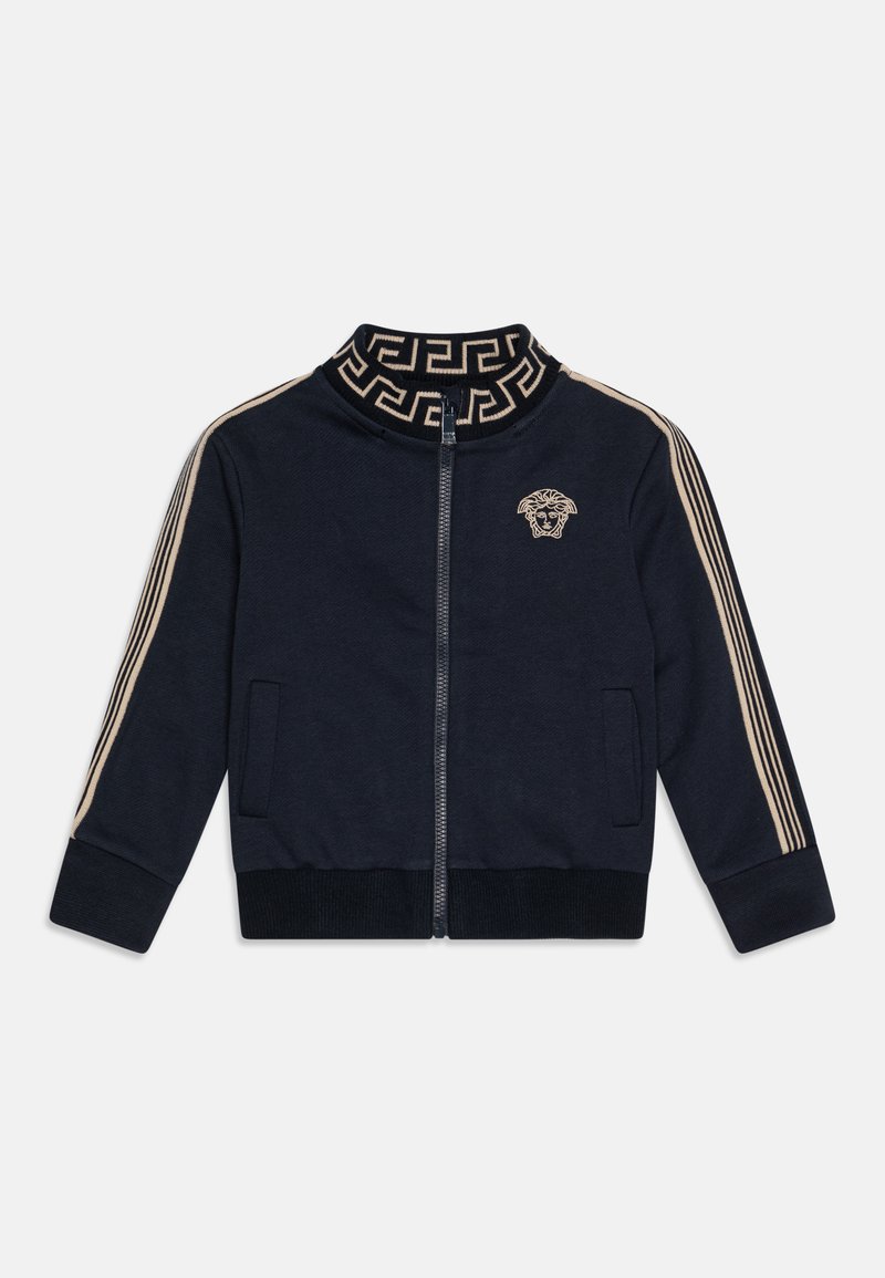 Navy zip-up jacket with high collar, gold graphic accents, and striped sleeves. Features side pockets and a lion emblem on the chest.