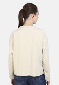 Lichtbeige trui met een ontspannen pasvorm, geribde halslijn en lange mouwen. Naadloos ontwerp aan de achterkant, gecombineerd met donkerblauwe spijkerbroek.