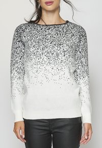 Pull blanc présentant un motif noir tacheté qui s'estompe dans la base blanche. Texture tricotée avec un col rond et des poignets côtelés.