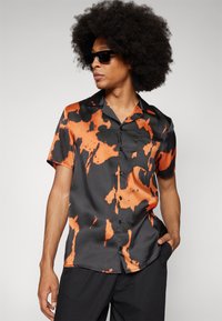 Korte mouwen shirt van glanzende stof met een zwart en oranje tie-dye patroon, een borstzak en een klassieke kraag.