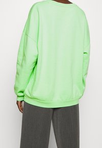 Översized sweatshirt i klar grön, tillverkad av mjuk bomullsblandning. Har nedhasade axlar, ribbade ärmslut och en avslappnad passform.