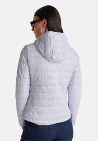 Světle levandulová péřová bunda s horizontálním prošíváním, s připevněnou kapucí a hladkým povrchem; kombinována s tmavými džínami.