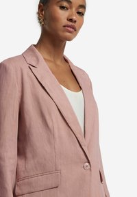 Ljusrosa blazer med en slät textur, skräddarsydd design, notchade slag, enkel knäppning och sidfickor.