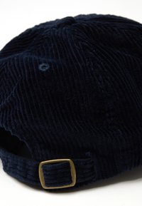Gorra de pana azul marino con correa ajustable de hebilla de latón, destacando la textura y el detalle sobre un fondo blanco.