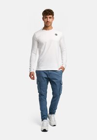 Langærmet hvid skjorte med et lille logo på brystet, parret med blå cargo-bukser med lommer og en smal pasform.